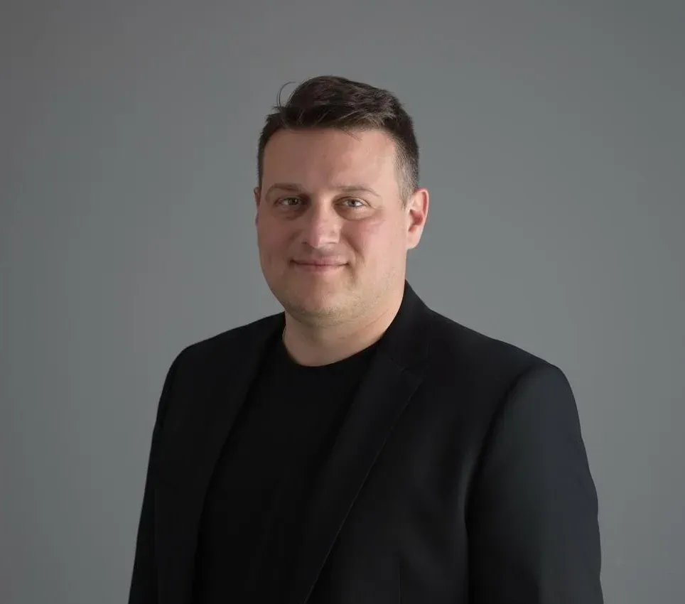 Nico Santangelo, portrait in a dark blazer against a grey studio background